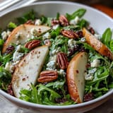 A light balsamic dressing glistens over the vibrant Arugula and Pear Bowl, ready to serve as a refreshing lunch.