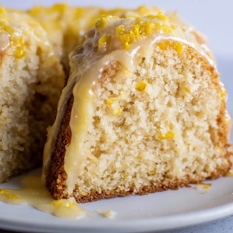 Overhead view of a freshly glazed Lemon Pound Cake with bright lemon zest and juice, its surface glistening and ready to slice.
