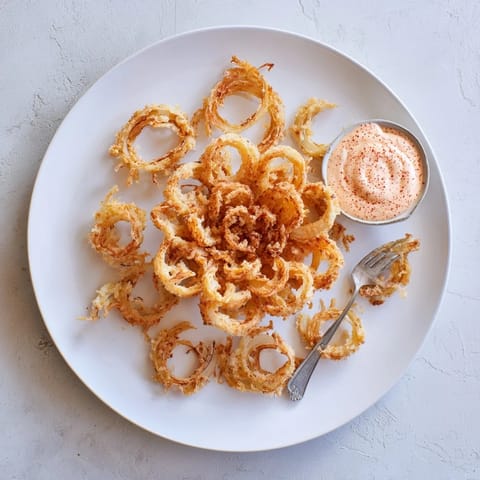 A close-up view of crispy, battered Onion Petals dipped in zesty sauce, perfect for sharing at a party or game day.