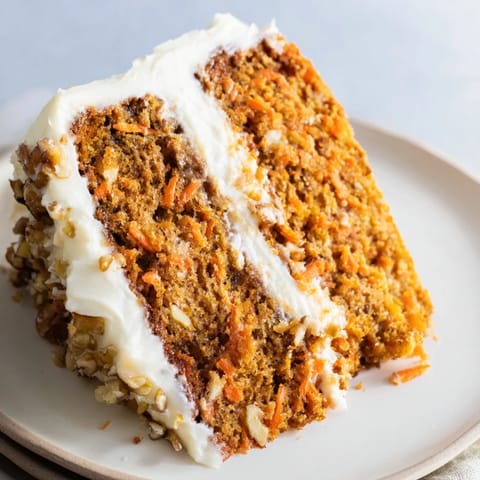 A close-up of frosted Carrot Cake showing moist crumb and chopped pecans on top.