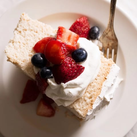 A slice of fluffy Angel Food Cake topped with fresh strawberries and a dollop of whipped cream.
