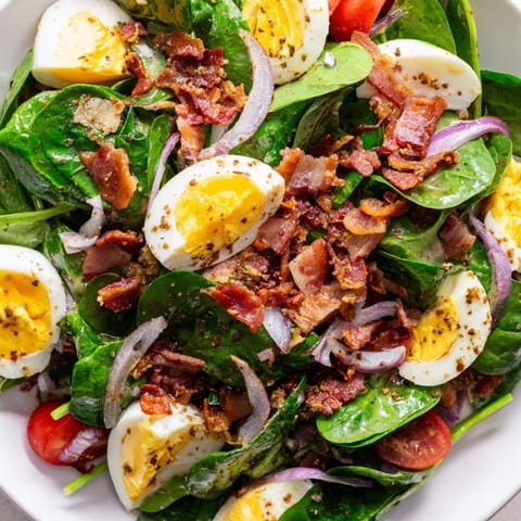 Sliced boiled eggs and crunchy bacon over a bed of fresh spinach, with a tangy homemade dressing perfect for a satisfying light lunch.