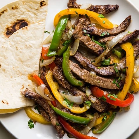 Colorful steak fajitas on a platter with sautéed peppers and onions, alongside fresh toppings and lime wedges.