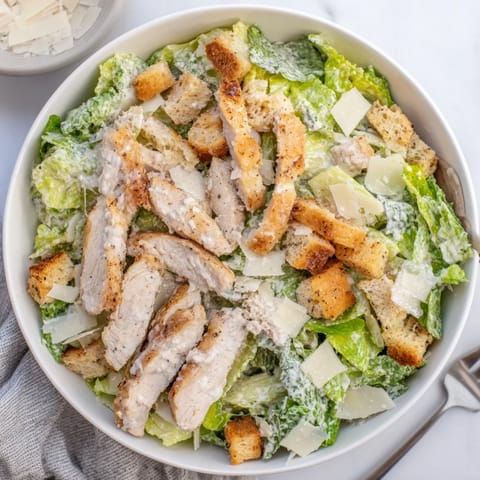 Crunchy croutons and shaved Parmesan top a classic Chicken Caesar Salad plated with extra dressing on the side.