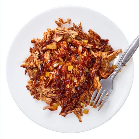 Shredded BBQ Pulled Chicken served hot over creamy grits, garnished with fresh parsley.