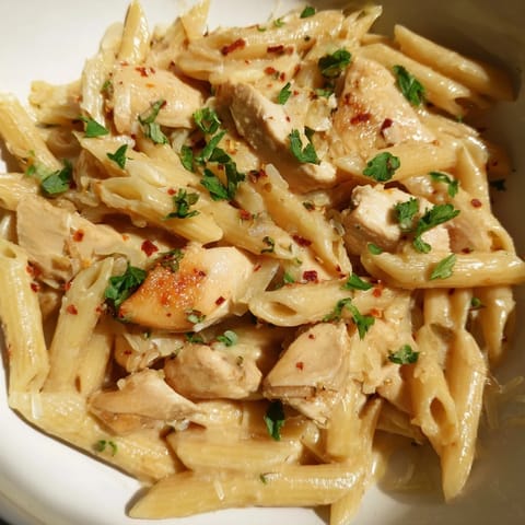 A close-up of golden roasted garlic chicken penne with steam rising from the skillet.  