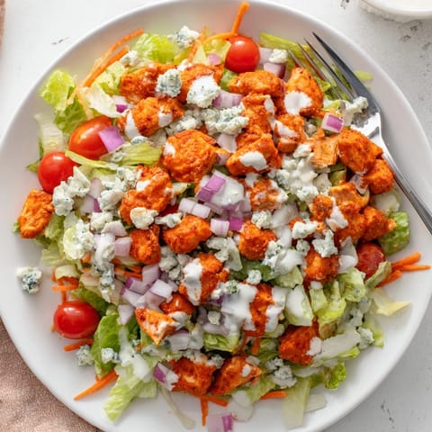 A hearty Buffalo Chicken Chopped Salad is ready to serve, garnished with red onion and shredded carrots for extra crunch.