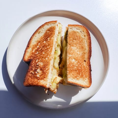 Two halves of a Havarti & Caramelized Leek Grilled Cheese rest beside a fresh green salad.