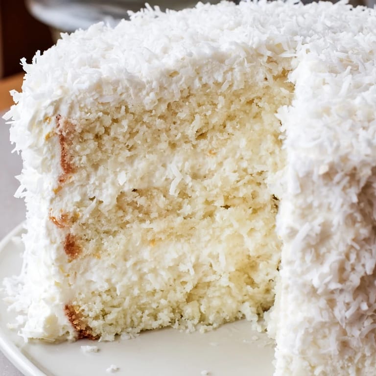 A close-up of Coconut Cake reveals fluffy meringue frosting and tender layers filled with sweet coconut cream.