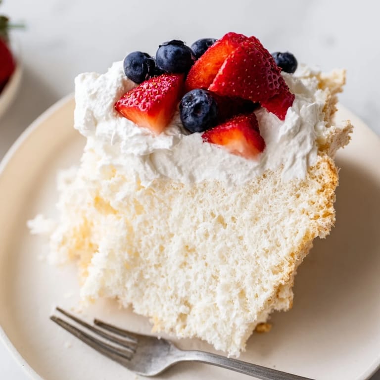 Golden-brown Angel Food Cake with a light, airy crumb sitting next to a bowl of mixed berries.