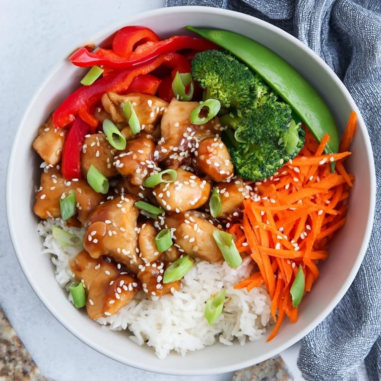 Sizzling teriyaki chicken bowl topped with crisp sugar snap peas, carrots, and red bell peppers, garnished with fresh green onions for a vibrant dinner.