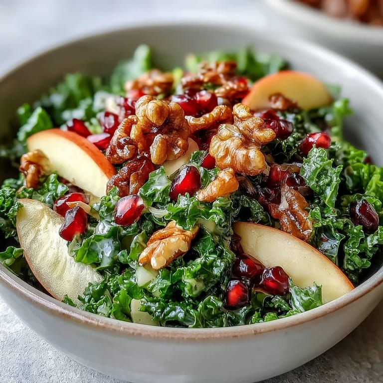 Colorful ingredients for a healthy Kale and Pomegranate Bowl arranged in a white bowl, featuring chopped kale, sliced apples, and ruby-red pomegranate arils.