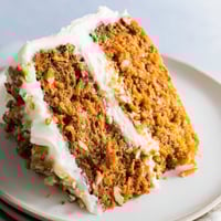 A close-up of frosted Carrot Cake showing moist crumb and chopped pecans on top.